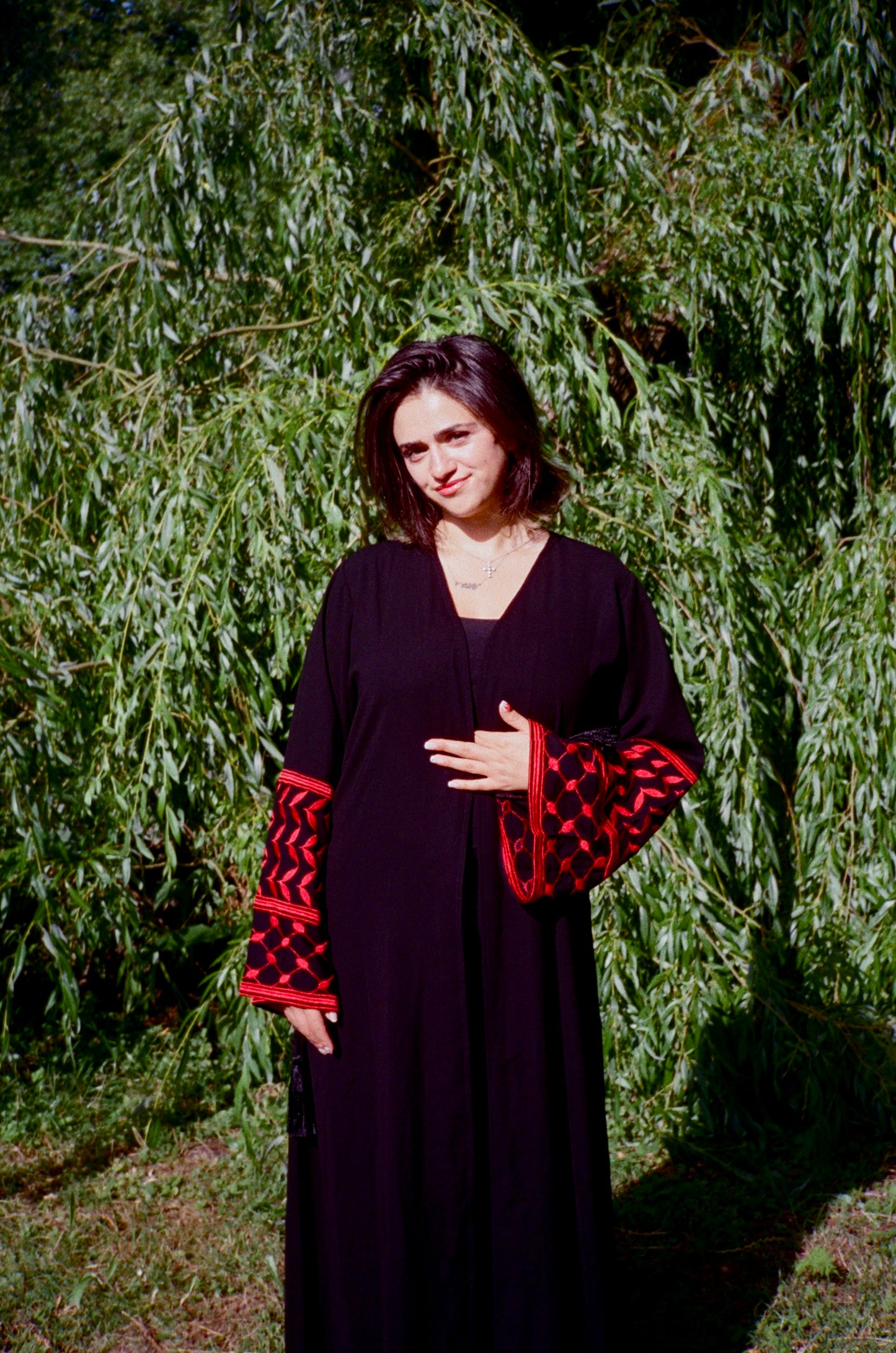 Woman wearing a black dress with red patterns standing in front of green foliage