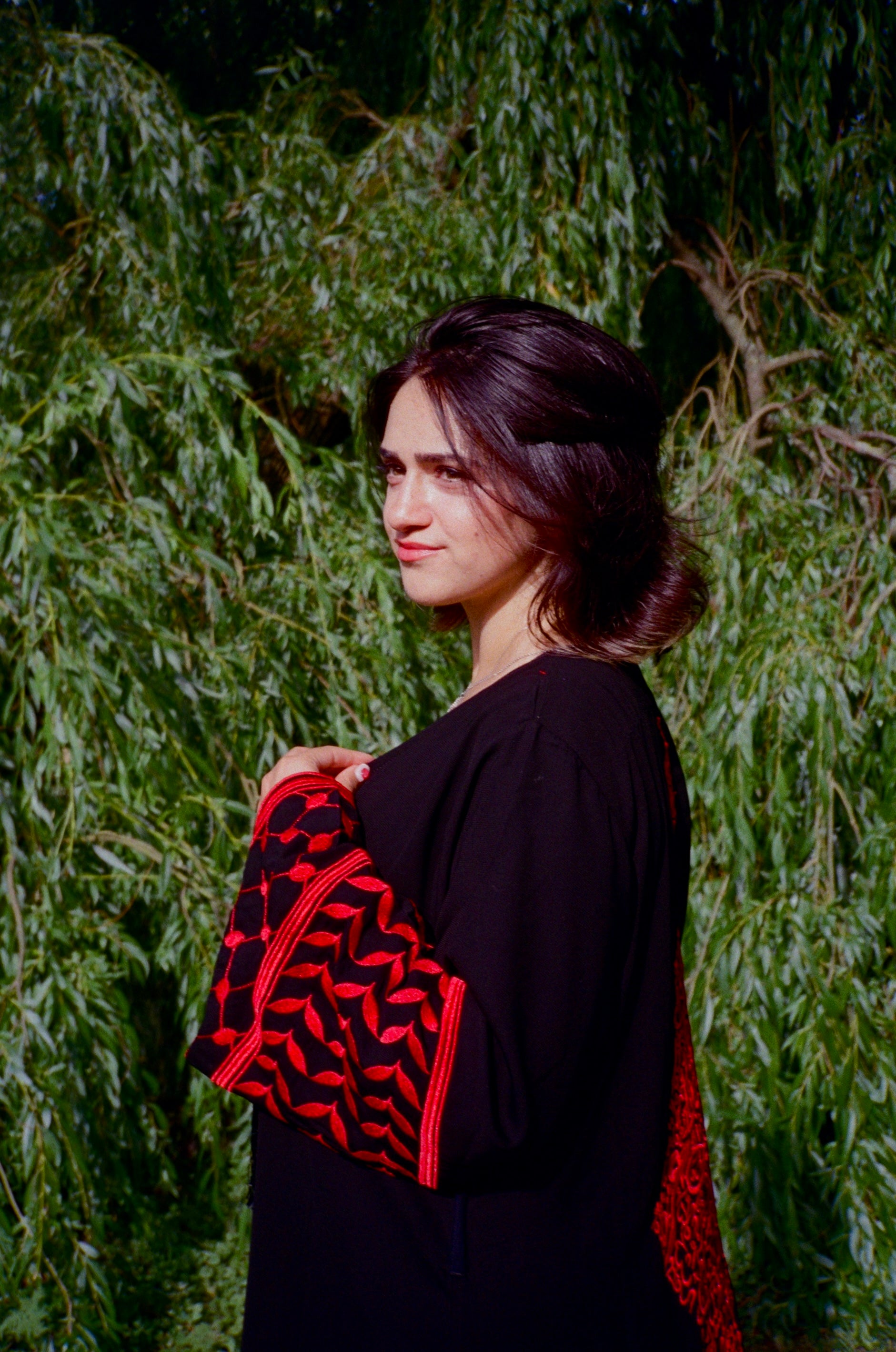 Woman wearing a black outfit with red and black patterned sleeves against a green leafy background