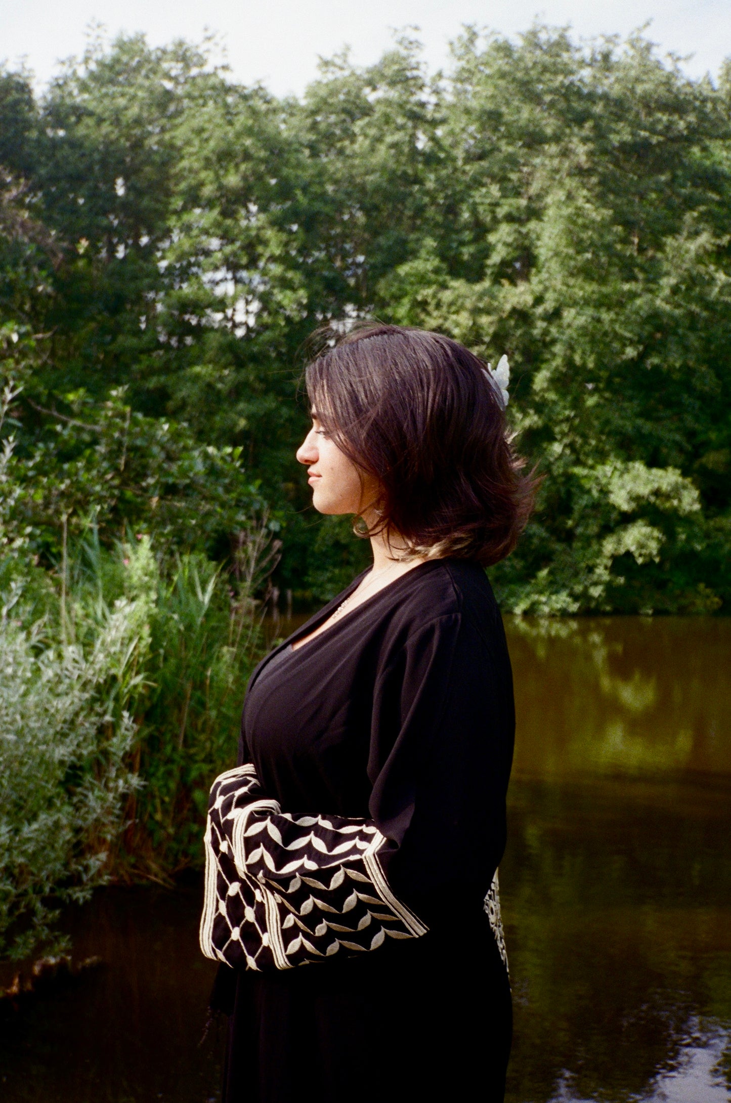 Woman standing by a body of water with trees in the background
