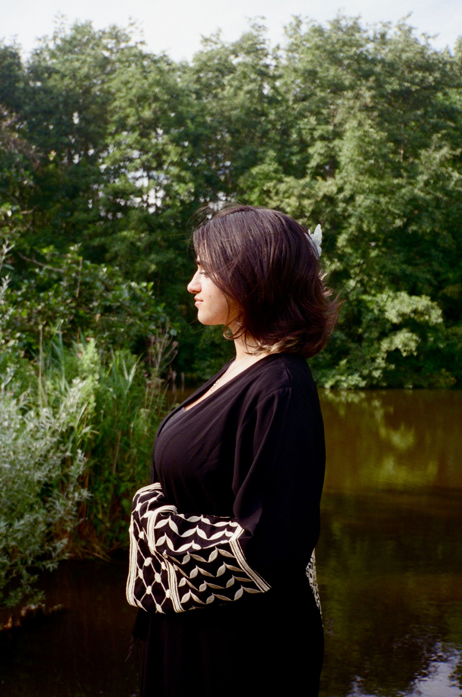Woman standing by a body of water with trees in the background