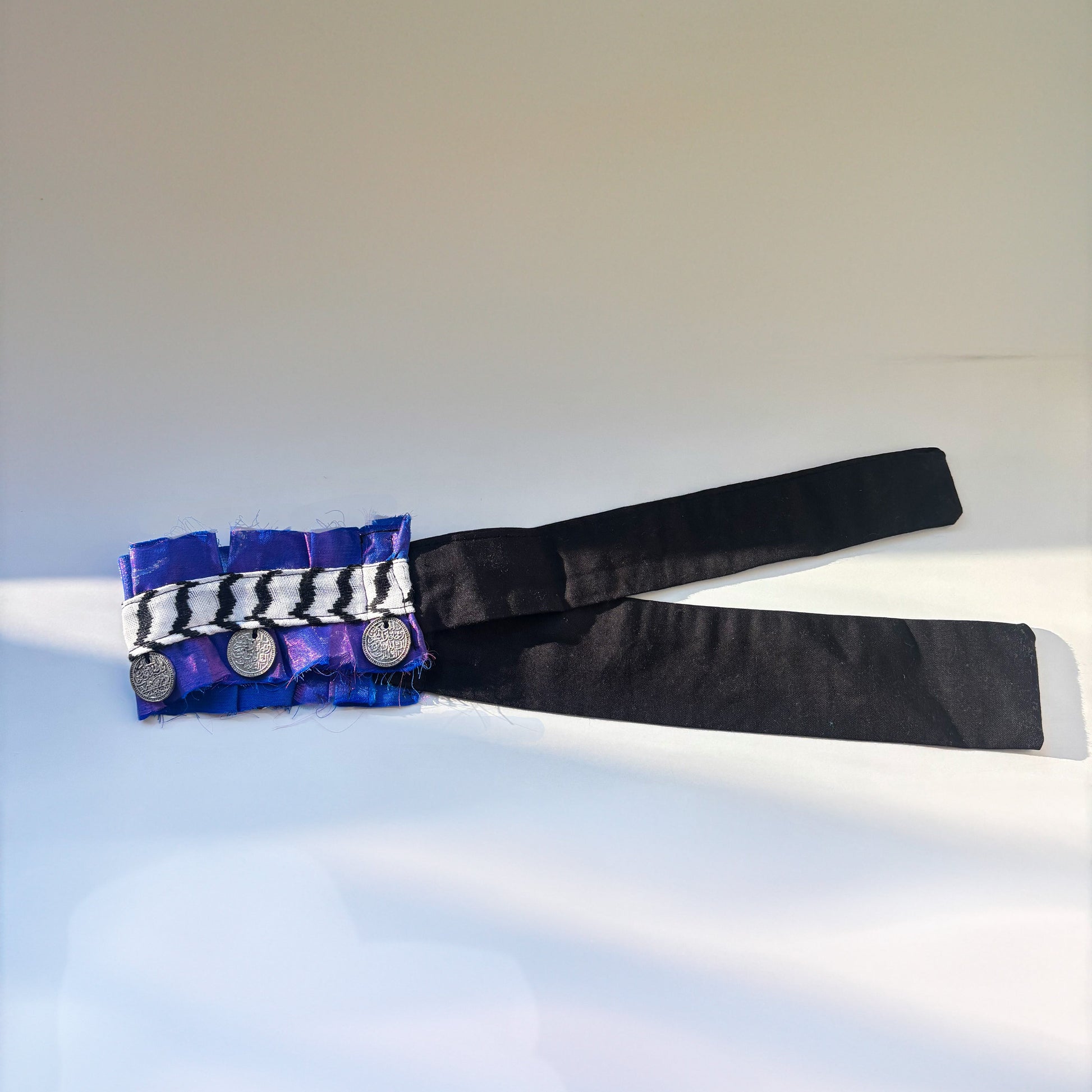 Black necklace with a blue, purple, silver decorative coin necklace on a light gray background