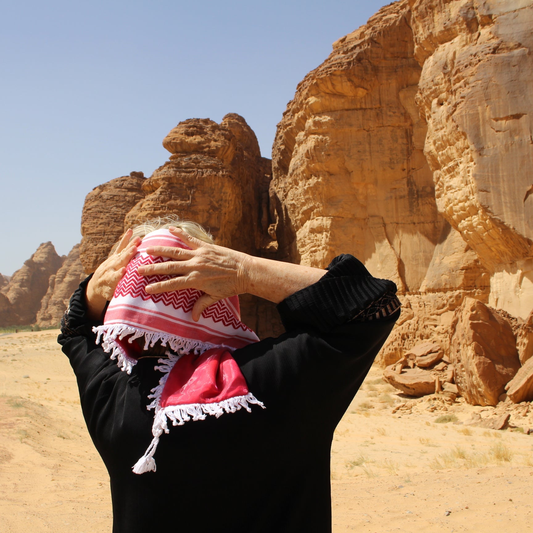 Woman wearing beautiful red keffiyeh scarf in al ula desert saudi arabia