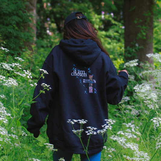 Person wearing a black hoodie with text walking through a field of white flowers in a forest