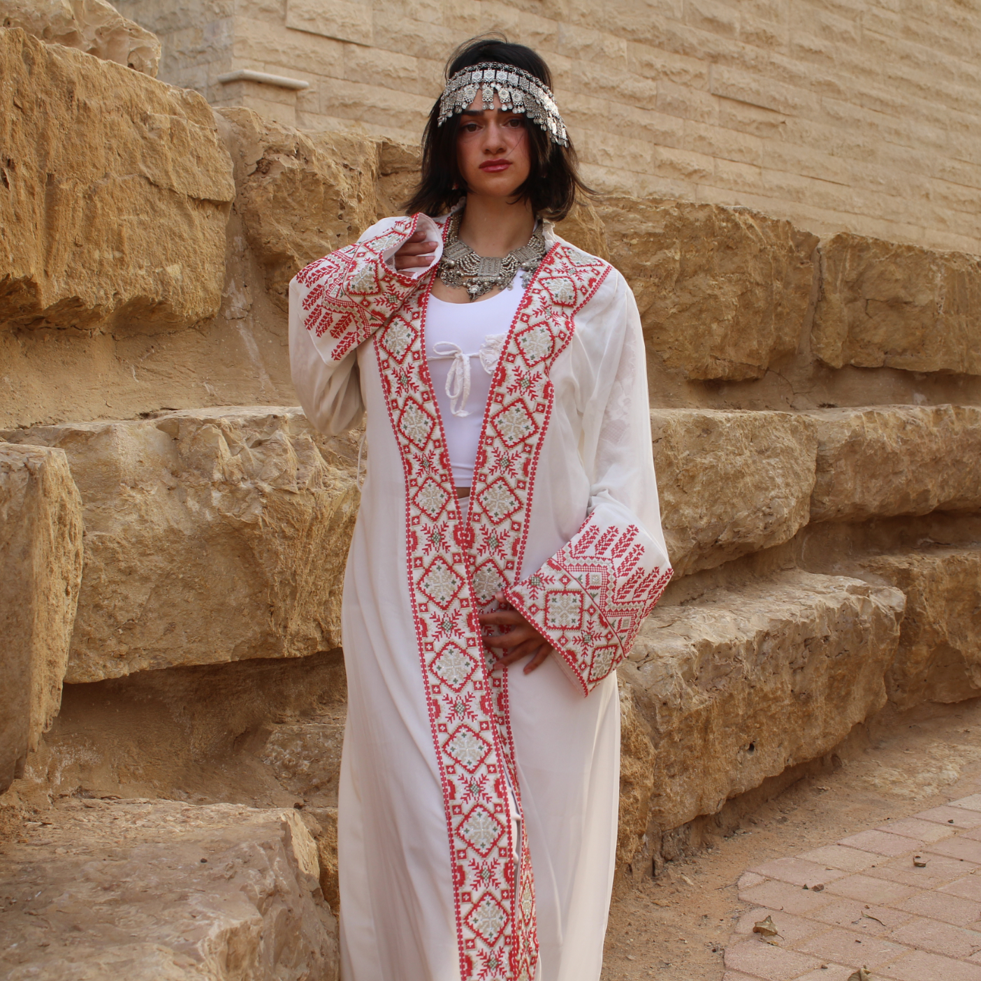 Woman in traditional tatreez outfit standing in front of stone wall