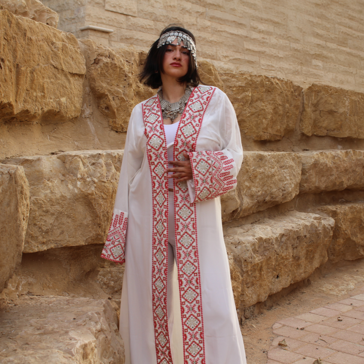 Woman in a traditional outfit tatreez standing in front of stone ruins